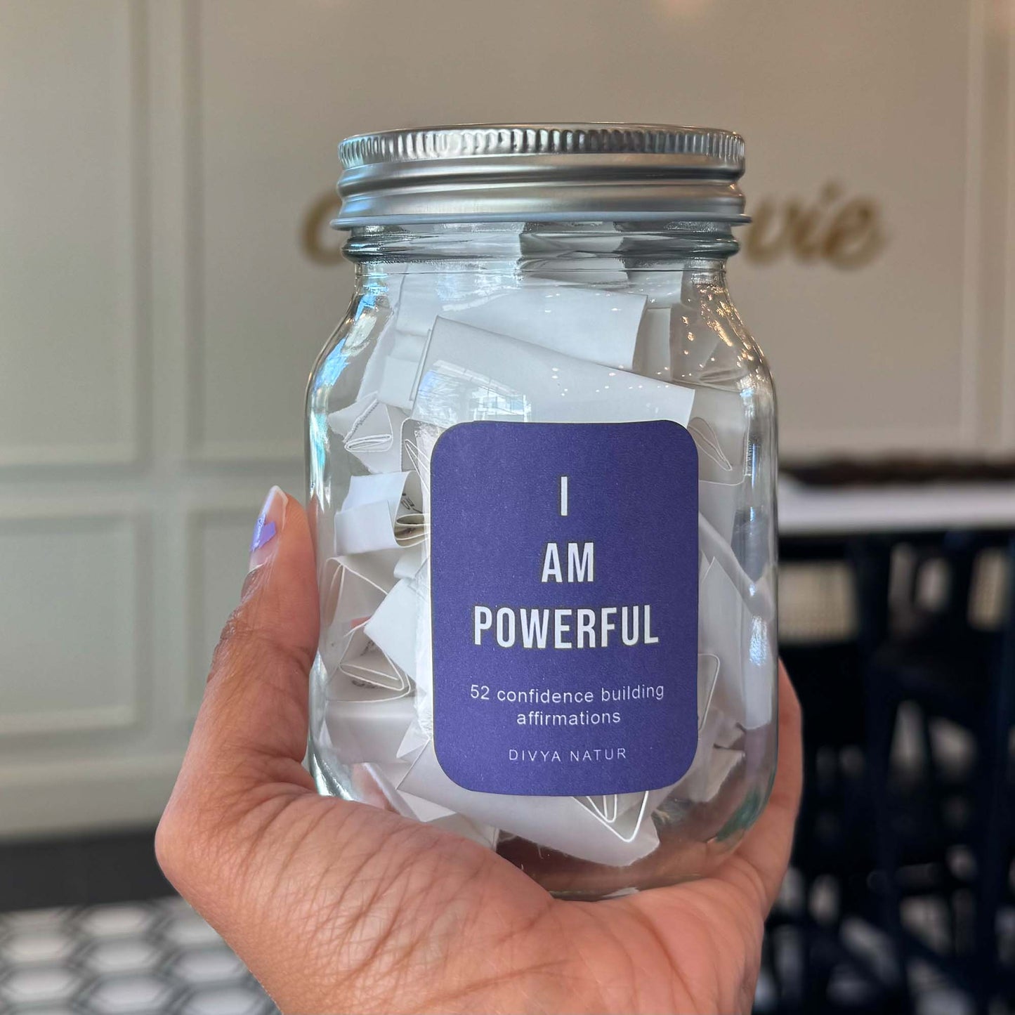 Hand holding a jar with 'I AM POWERFUL' affirmation cards and a purple label.