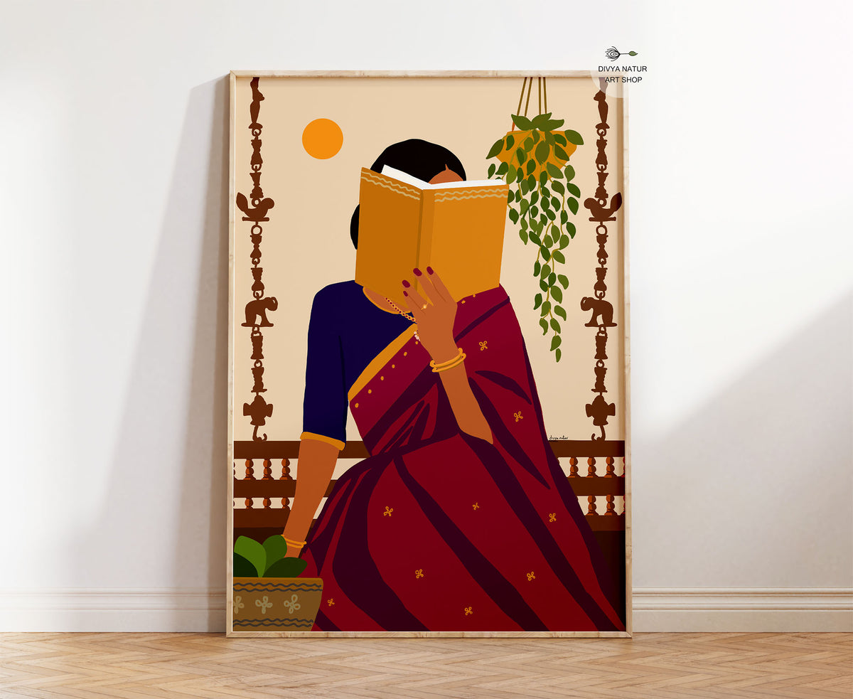 A framed art print leaning against a white wall on a light wood floor. The print features a stylized illustration of a woman in a deep red and navy blue sari, holding a yellow book to her face, with a hanging green plant and a yellow sun in the background.