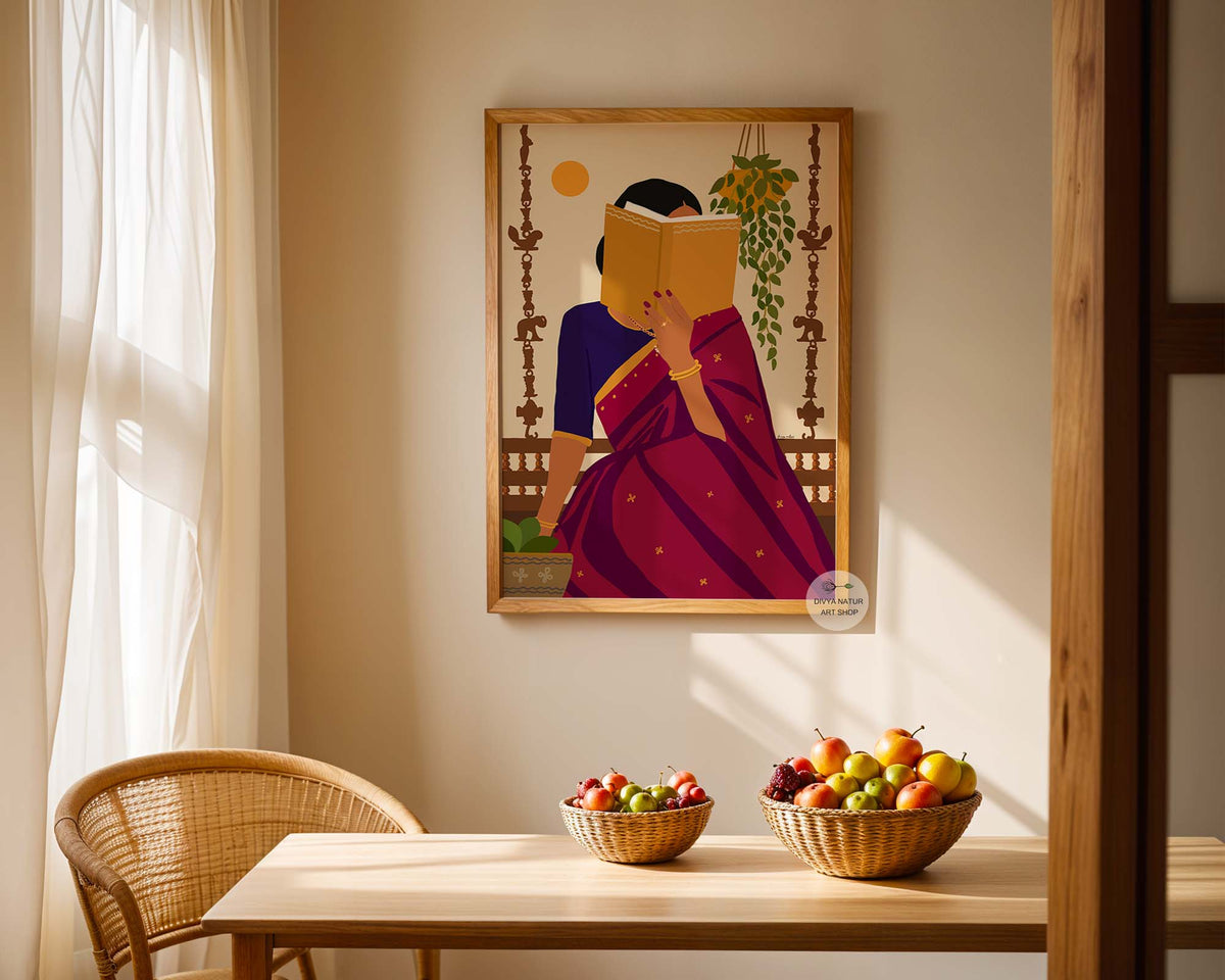 A framed art print depicting a woman in a purple and pink sari reading a yellow book, hanging on a beige wall above a wooden dining table with fruit bowls and a wicker chair.