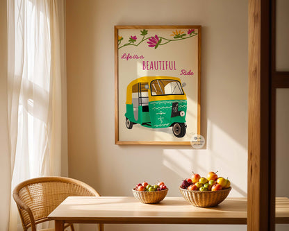 Framed artwork of a green and yellow auto-rickshaw with 'Life is a Beautiful Ride' text on a wall above a table with fruit bowls.