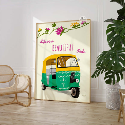 Framed artwork with a green and yellow auto-rickshaw and 'Life is a Beautiful Ride' text in a room with a plant and chair.